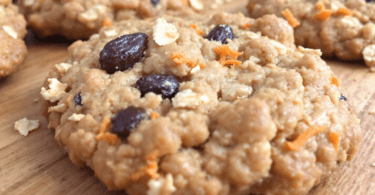 A close-up image of freshly baked oatmeal raisin cookies with visible carrot shreds, placed on a rustic wooden table.