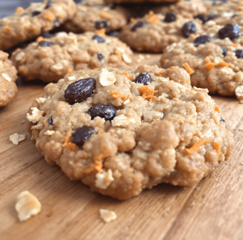 A close-up image of freshly baked oatmeal raisin cookies with visible carrot shreds, placed on a rustic wooden table.