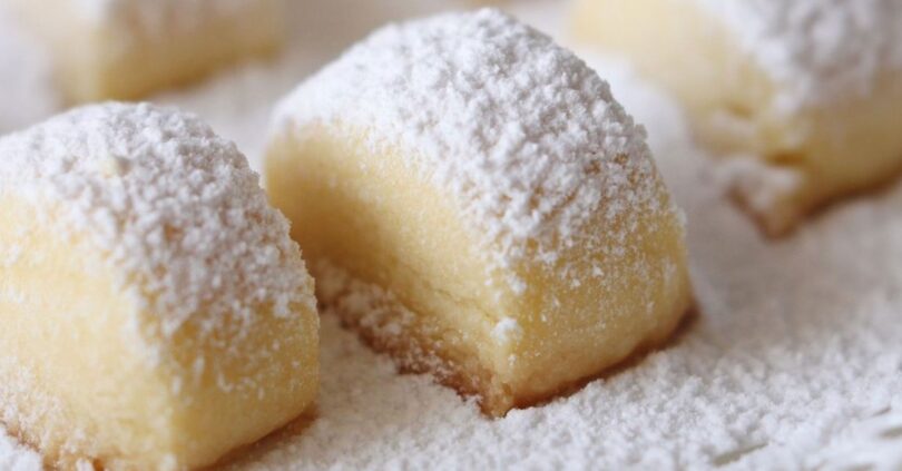 A plate of small, buttery Melting Moments cookies, dusted with confectioners' sugar and garnished with fresh raspberries.