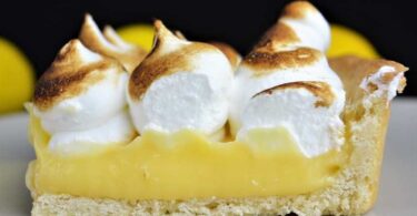 A slice of Grandma's Magic Lemon Pie on a plate, with a dollop of whipped cream on top.