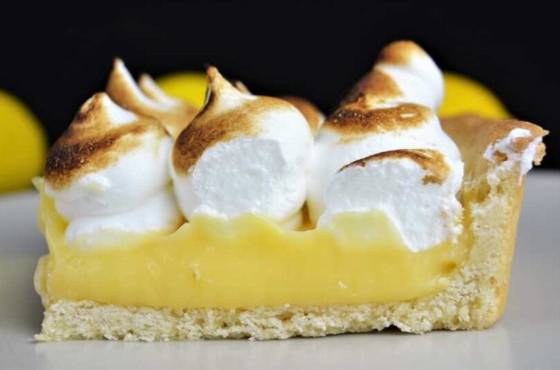 A slice of Grandma's Magic Lemon Pie on a plate, with a dollop of whipped cream on top.