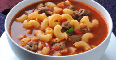 A steaming bowl of hearty Beefy Tomato Macaroni Soup, filled with tender ground beef, flavorful diced tomatoes, and al dente macaroni. Topped with grated cheddar cheese and served with a side of crusty bread. Perfect for a cold winter day or a comforting meal.