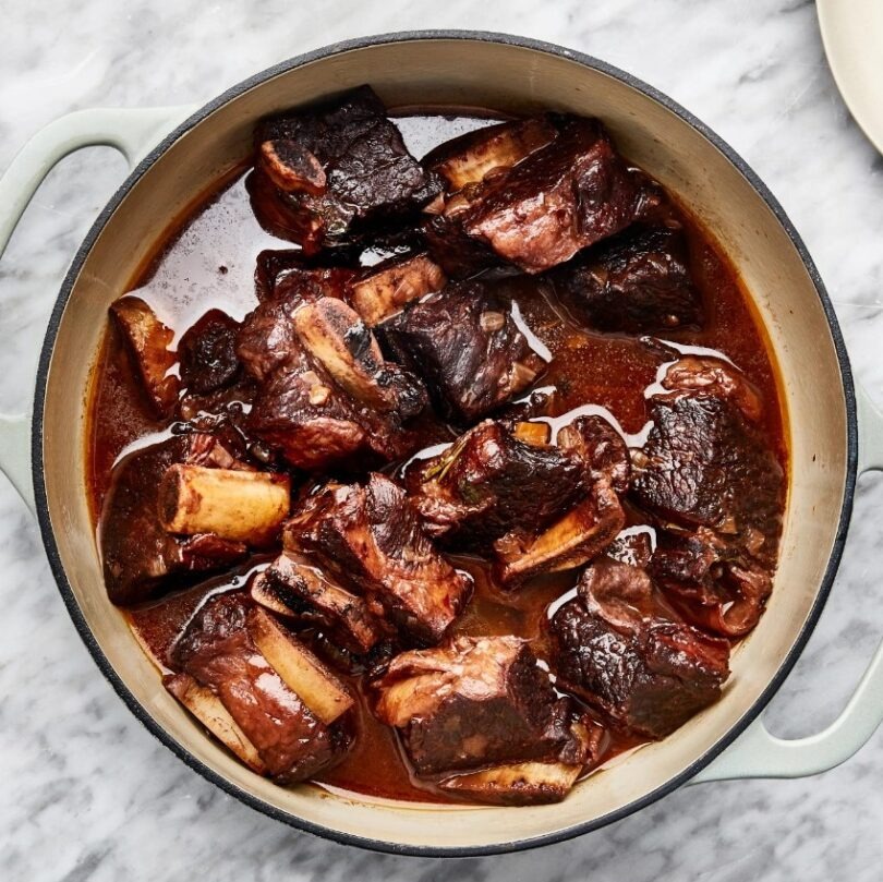 A plate of juicy and tender braised short ribs, slow-cooked in a flavorful sauce, with a side of creamy mashed potatoes.