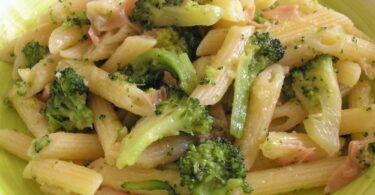 A plate of penne pasta with broccoli, tuna, and broccoli cheddar sauce, topped with Parmesan cheese.