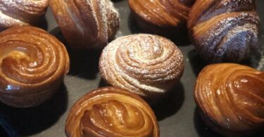 A close-up photo of a freshly baked cruffin with layers of flaky pastry and cinnamon-sugar filling, on a rustic background.