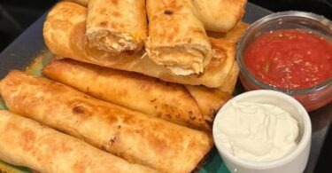 A plate of golden brown and crispy chicken taquitos cooked in an Air Fryer with toppings on the side.