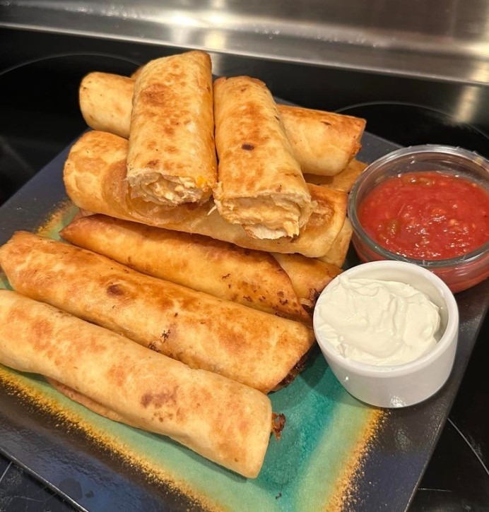 A plate of golden brown and crispy chicken taquitos cooked in an Air Fryer with toppings on the side.