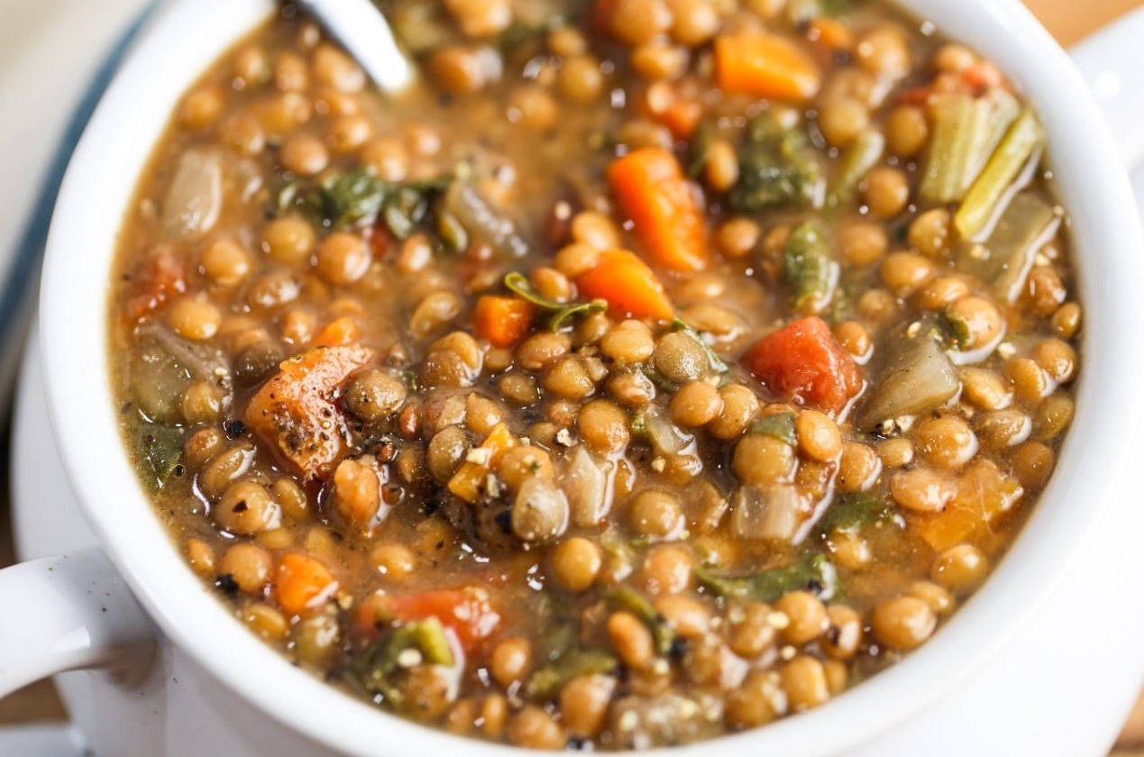 A bowl of steaming stewed lentils garnished with herbs and served with slices of crusty bread