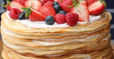 A photo of a stacked crepe cake with pastry cream filling and powdered sugar dusted on top.