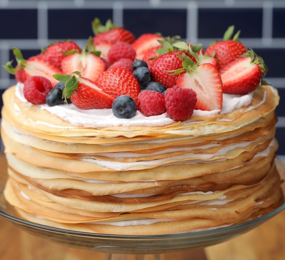 A photo of a stacked crepe cake with pastry cream filling and powdered sugar dusted on top.