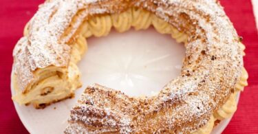 A round pastry filled with praline cream and sliced almonds on top, with powdered sugar sprinkled over it.