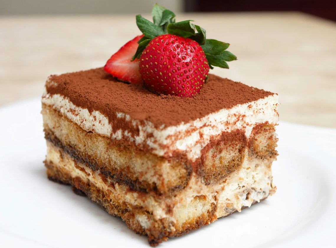 A slice of classic tiramisu on a plate with cocoa powder on top.