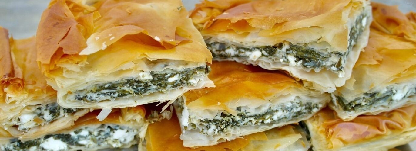 A triangular shaped pastry filled with spinach and feta cheese, with layers of phyllo dough on top and bottom. Spanakopita is a popular Greek savory pastry made with spinach, feta cheese, and layers of phyllo dough. This delicious dish is often served as an appetizer or snack, and is a favorite among vegetarians and non-vegetarians alike. The filling is seasoned with herbs and spices, giving it a flavorful taste and aroma. Try making Spanakopita at home for a tasty and impressive dish that's sure to impress your guests!