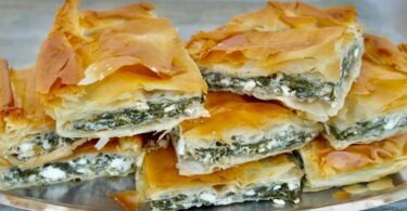 A triangular shaped pastry filled with spinach and feta cheese, with layers of phyllo dough on top and bottom.