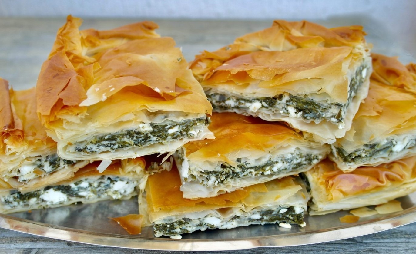 A triangular shaped pastry filled with spinach and feta cheese, with layers of phyllo dough on top and bottom. Spanakopita is a popular Greek savory pastry made with spinach, feta cheese, and layers of phyllo dough. This delicious dish is often served as an appetizer or snack, and is a favorite among vegetarians and non-vegetarians alike. The filling is seasoned with herbs and spices, giving it a flavorful taste and aroma. Try making Spanakopita at home for a tasty and impressive dish that's sure to impress your guests!