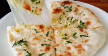 Image of cheese stuffed naan bread on a plate - Learn how to make delicious cheese-stuffed naan bread with this easy recipe. Soft, pillowy bread filled with cheddar and parmesan cheese, brushed with garlic and parsley oil. Perfect as a side dish or a snack.