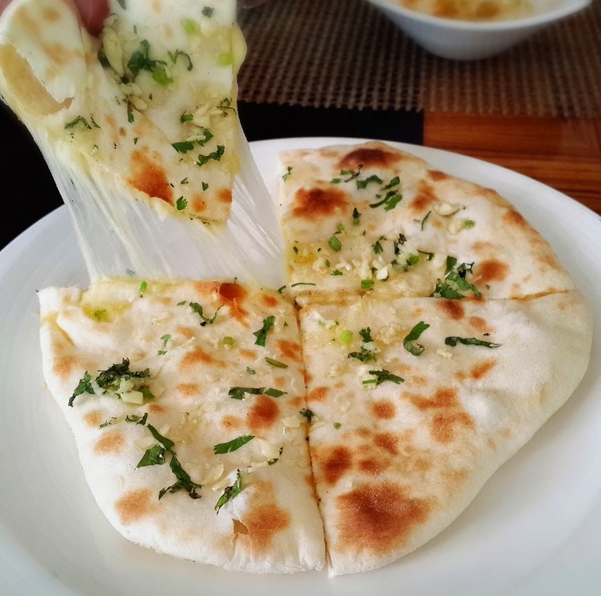 Image of cheese stuffed naan bread on a plate - Learn how to make delicious cheese-stuffed naan bread with this easy recipe. Soft, pillowy bread filled with cheddar and parmesan cheese, brushed with garlic and parsley oil. Perfect as a side dish or a snack.
