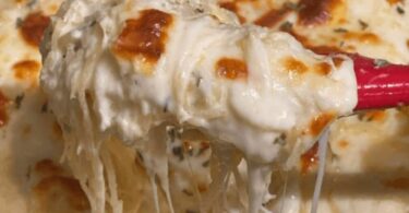 A delicious plate of chicken spaghetti topped with melted cheese and served with garlic bread and salad.