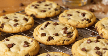 A freshly baked batch of classic chocolate chip cookies on a cooling rack, showcasing their golden-brown edges and melted chocolate chips, with a glass of milk in the background.