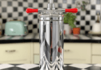 An elegant vintage soda siphon with a chrome body and bright red handles, reminiscent of mid-20th century design, sitting on a retro kitchen counter.